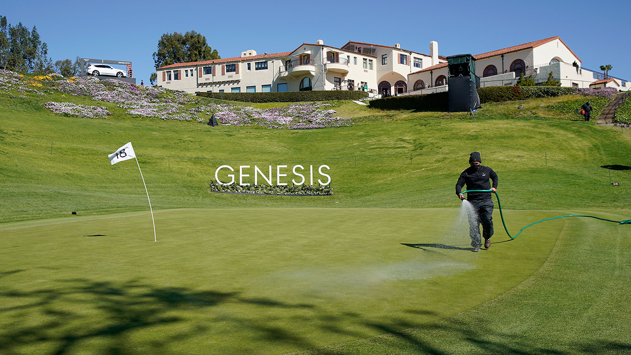 The pin flag for the 18th green bends over from the wind as a greenskeeper waters the grass after high winds suspended play during the third round of the Genesis Invitational golf tournament at Riviera Country Club, Saturday, Feb. 20, 2021, in the Pacific Palisades area of Los Angeles. (Ryan Kang/AP)