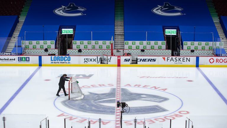 An arena worker removes the net from the ice after the Vancouver Canucks and Calgary Flames NHL hockey game was postponed due to a positive COVID-19 test result, in Vancouver, on Wednesday, March 31, 2021. (Darryl Dyck/CP)