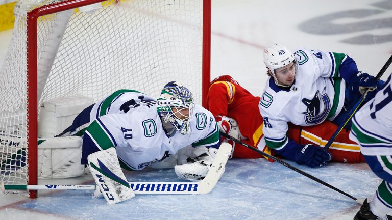 Vancouver Canucks goalie Braden Holtby, left, and Quinn Hughes, right, crash into the net with Calgary Flames' Elias Lindholm from scoring during third period NHL hockey action in Calgary, Wednesday, May 19, 2021. (Jeff McIntosh/CP)