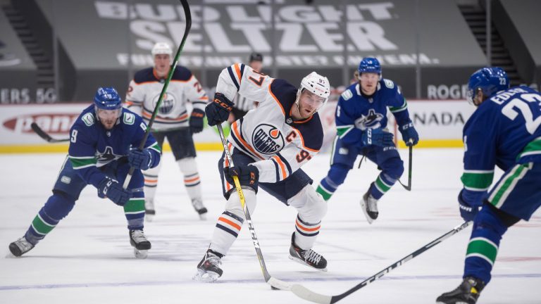 Edmonton Oilers' Connor McDavid (97) stickhandles past Vancouver Canucks' J.T. Miller (9) and Alexander Edler (23), of Sweden, during the first period of an NHL hockey game in Vancouver, B.C., Monday, May 3, 2021. THE CANADIAN PRESS/Darryl Dyck