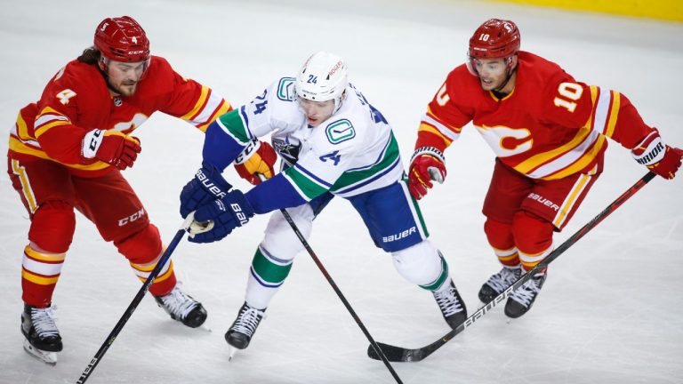 Vancouver Canucks' Jimmy Vesey, centre, is checked by Calgary Flames' Rasmus Andersson, left, and Derek Ryan during second period NHL hockey action in Calgary, Wednesday, May 19, 2021. (Jeff McIntosh/CP)