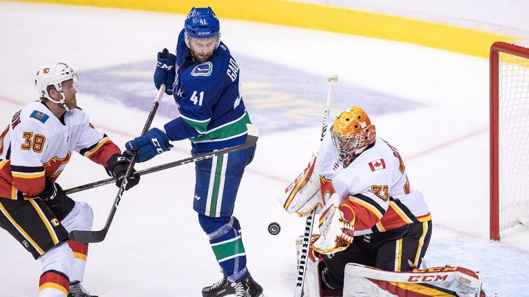 Former Calgary Flames goalie David Rittich, of the Czech Republic, makes a save as Philip Samuelsson (38), of Sweden, checks Vancouver Canucks' Jonah Gadjovich (41). (Darryl Dyck/CP)