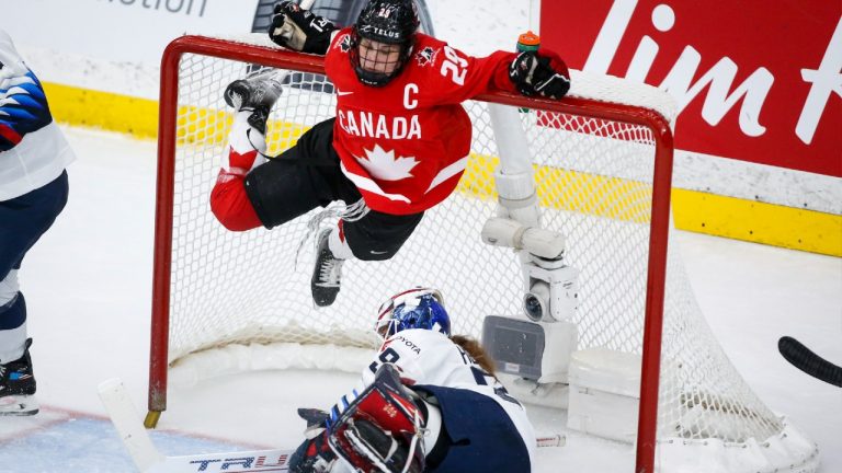 Canada's Marie-Philip Poulin, top, hangs from the cross bar after crashing into goalie Nicole Hensley, of the United States, during third period gold medal final IIHF Women's World Championship hockey action in Calgary, Tuesday, Aug. 31, 2021 (Jeff McIntosh/CP).