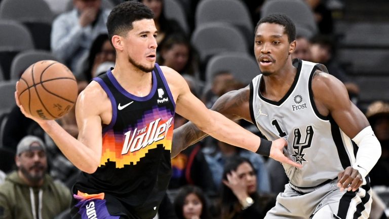 Phoenix Suns' Devin Booker, left, looks to pass the ball as he is defended by San Antonio Spurs' Lonnie Walker IV during the first half of an NBA basketball game, Monday, Nov. 22, 2021, in San Antonio. (Darren Abate/AP) 