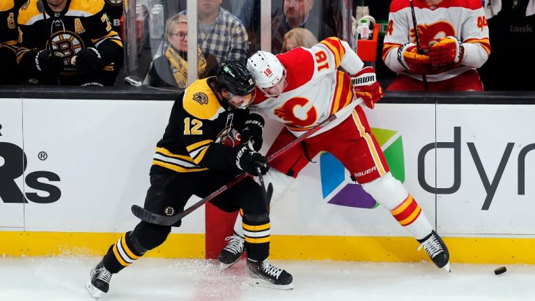 Boston Bruins' Craig Smith (12) and Calgary Flames' Tyler Pitlick (18) battle for the puck during the second period of an NHL hockey game, Sunday, Nov. 21, 2021, in Boston. (Michael Dwyer/AP Photo) 
