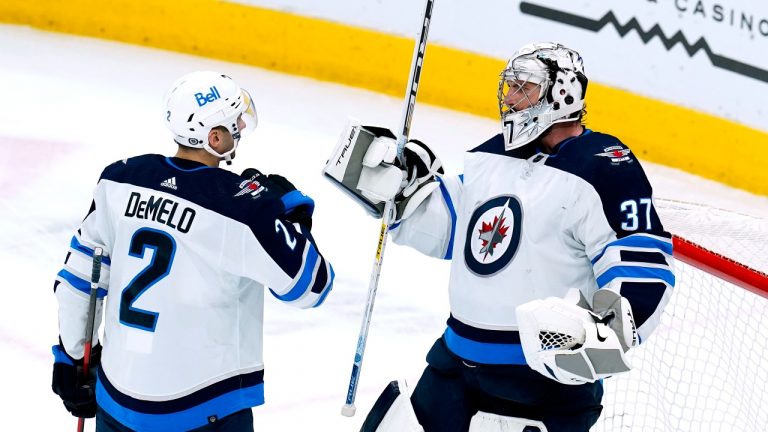 Winnipeg Jets goaltender Connor Hellebuyck (37) and defenseman Dylan DeMelo (2) celebrate at the end of the team's NHL hockey game against the Arizona Coyotes on Tuesday, Jan. 4, 2022, in Glendale, Ariz. The Jets won 3-1. (Ross D. Franklin/AP Photo) 
