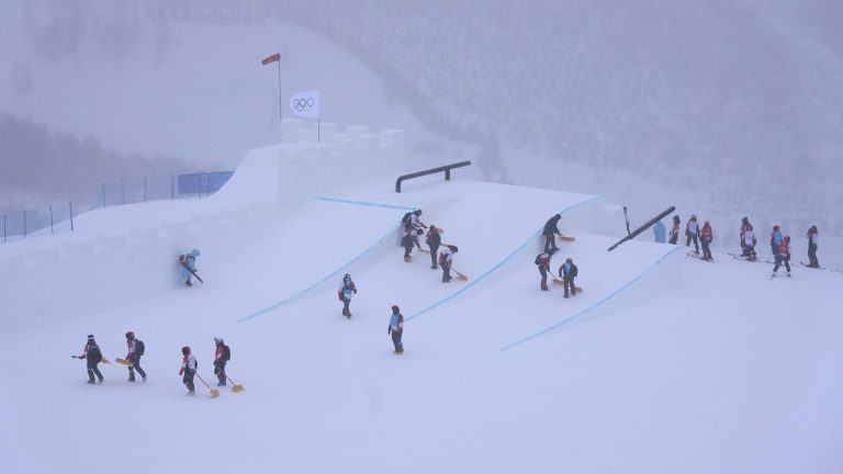 Volunteers clear the course as the start of the women's slopestyle qualification has been delayed due to a weather consition at the 2022 Winter Olympics. (AP Photo/Francisco Seco)