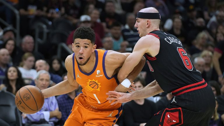 Phoenix Suns guard Devin Booker (1) drives on Chicago Bulls guard Alex Caruso during the second half of an NBA basketball game Friday, March 18, 2022, in Phoenix. Phoenix won 129-102. (AP Photo/Rick Scuteri)