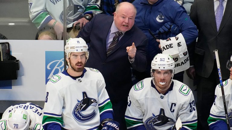 Vancouver Canucks coach Bruce Boudreau, back, argues for a call with an official, while standing behind right wing Conor Garland, front left, and center Bo Horvat during the third period of the team's NHL hockey game against the Colorado Avalanche on Wednesday, March 23, 2022, in Denver. (David Zalubowski/AP)