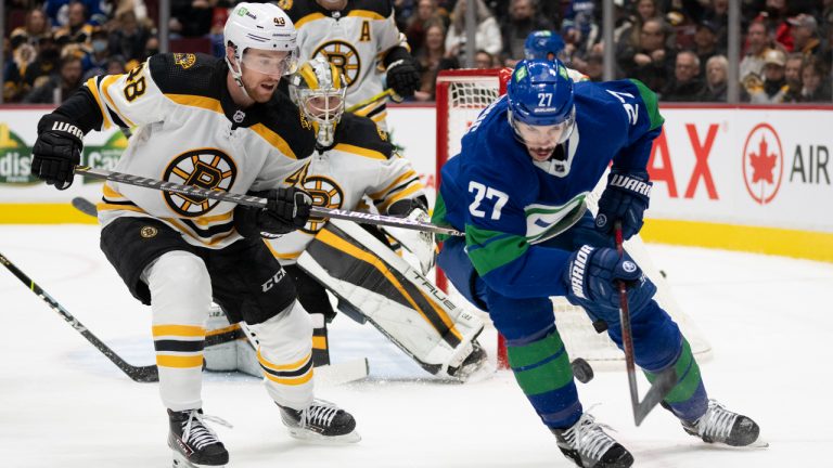 Boston Bruins defenceman Matt Grzelcyk (48) fights for control of the puck with Vancouver Canucks defenceman Travis Hamonic (27) during second period NHL action in Vancouver, Wednesday, December 8, 2021. (Jonathan Hayward/CP)