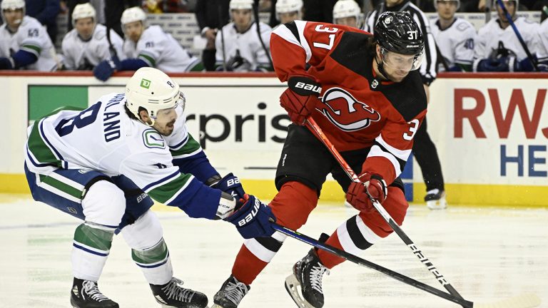 New Jersey Devils center Pavel Zacha (37) handles the puck as he is checked by Vancouver Canucks right wing Conor Garland (8) during the first period of an NHL hockey game. (Bill Kostroun/AP)