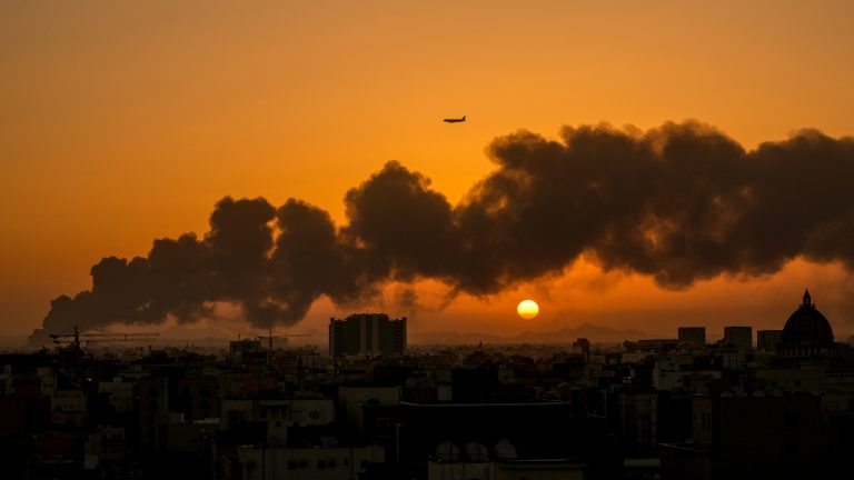 A passenger airplane flies over a smouldering fire at a Saudi Aramco oil depot after a Yemen Houthi rebel attack, ahead of a Formula One race as the sun rises in Jiddah, Saudi Arabia, Saturday, March 26, 2022. (Hassan Ammar/AP)