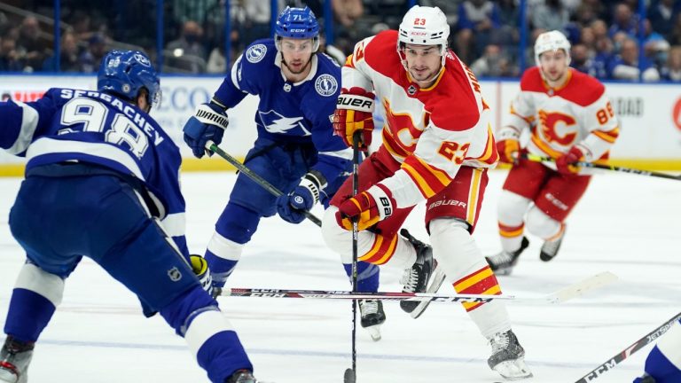 Calgary Flames center Sean Monahan (23) moves the puck between Tampa Bay Lightning defenseman Mikhail Sergachev (98) and center Anthony Cirelli (71) during the first period of an NHL hockey game Thursday, Jan. 6, 2022, in Tampa, Fla. (Chris O'Meara/AP)