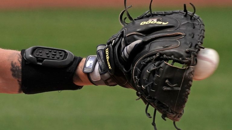 Seattle Mariners catcher Tom Murphy wears a wrist-worn device used to call pitches as he catches a ball during the sixth inning of a spring training baseball game against the Kansas City Royals, Tuesday, March 29, 2022, in Peoria, Ariz. The MLB is experimenting with the PitchCom system where the catcher enters information on a wrist band with nine buttons which is transmitted to the pitcher to call a pitch. (Charlie Riedel/AP)