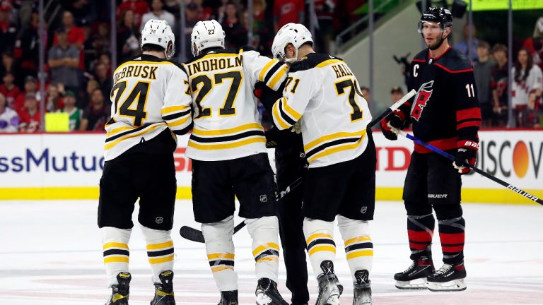 Boston Bruins' Hampus Lindholm (27) is helped from the ice by Jake DeBrusk (74) and Taylor Hall (71) as Carolina Hurricanes' Jordan Staal (11) watches during the second period of Game 2 of an NHL hockey Stanley Cup first-round playoff series in Raleigh, N.C., Wednesday, May 4, 2022. (Karl B DeBlaker/AP)