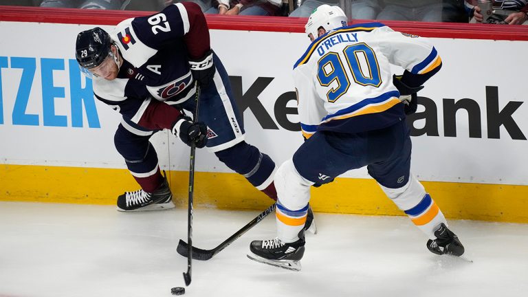 Colorado Avalanche center Nathan MacKinnon, left, struggles to control the puck as St. Louis Blues center Ryan O'Reilly defends in the first period of an NHL hockey game Tuesday, April 26, 2022, in Denver. (AP Photo/David Zalubowski)