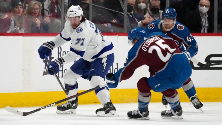 Tampa Bay Lightning center Anthony Cirelli, left, passes the puck past Colorado Avalanche right wing Logan O'Connor, front left, and center Darren Helm in the second period of an NHL hockey game Thursday, Feb. 10, 2022, in Denver. (David Zalubowski/AP)