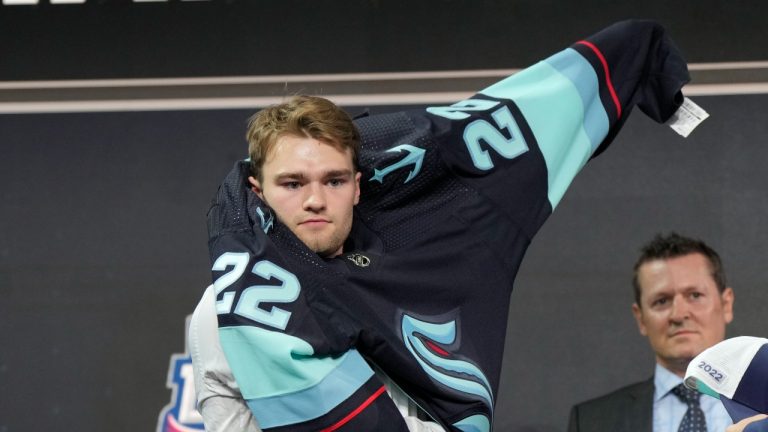 Shane Wright pulls on a Kraken jersey after being selected in the first round of the NHL draft by the Seattle Kraken in Montreal on Thursday, July 7, 2022. (Ryan Remiorz/THE CANADIAN PRESS)