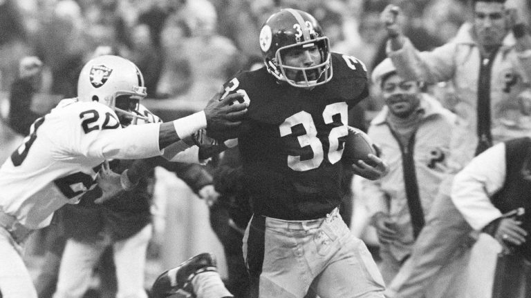 In this Dec. 23, 1972, file photo, Pittsburgh Steelers' Franco Harris (32) eludes a tackle by Oakland Raiders' Jimmy Warren as he runs 42-yards for a touchdown after catching a deflected pass during an AFC Divisional NFL football playoff game in Pittsburgh. The Pittsburgh Steelers announced on Tuesday, Sept. 6, 2022 they will retire the No. 32 of Hall of Fame running back Franco Harris during a Christmas Eve game against the Las Vegas Raiders. The honour will come 50 years and one day after Harris' iconic "Immaculate Reception" in a playoff victory over the Raiders. (Harry Cabluck/AP, File)