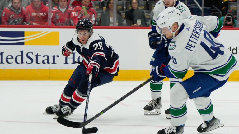 Washington Capitals right wing Connor Brown (28) and Vancouver Canucks center Elias Pettersson (40) reach for the puck during the first period of an NHL hockey game, Monday, Oct. 17, 2022, in Washington. (Jess Rapfogel/AP Photo)