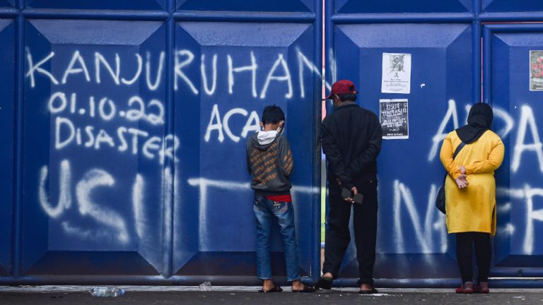 People peek inside one of the gates at Kanjuruhan Stadium where where a soccer stampede killed more than 100 people on Oct. 1, in Malang, East Java, Indonesia, Saturday, Oct. 8, 2022. Indonesia's president said the country will not face sanctions from soccer's world governing body and will remain the host of next year's U-20 World Cup after the firing of tear gas after a match inside the half-locked stadium caused the deadly crush at the exits. (Dicky Bisinglasi/AP)