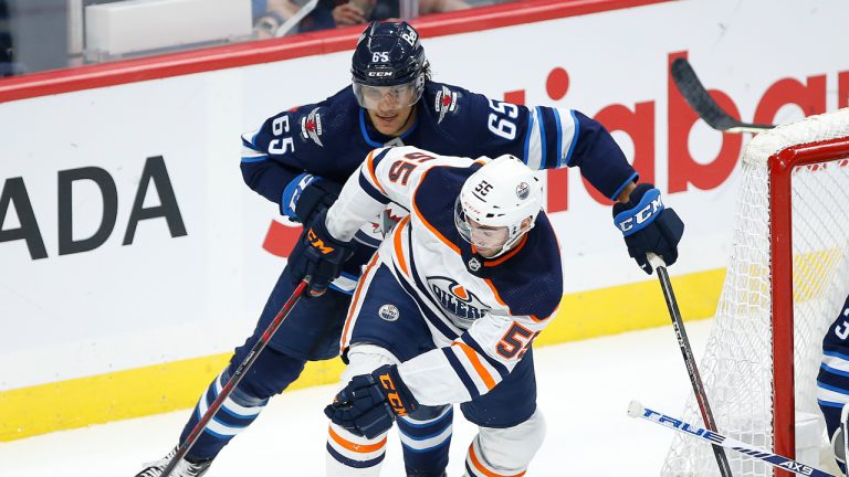 Winnipeg Jets' Johnathan Kovacevic (65) defends against Edmonton Oilers' Luke Esposito (55) as goaltender Connor Hellebuyck (37) looks on during second period pre-season NHL game action in Winnipeg on Wednesday, September 29, 2021. (John Woods/CP)