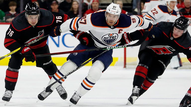 Edmonton Oilers' Connor McDavid (97) goes between Carolina Hurricanes' Brady Skjei (76) and Andrei Svechnikov (37) during the first period of an NHL hockey game in Raleigh, N.C., Sunday, Feb. 27, 2022. (AP Photo/Karl B DeBlaker)