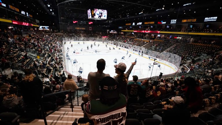 Fans watch players as they warm up prior to the Arizona Coyotes NHL home opening hockey game against the Winnipeg Jets at the 5,000 seat Mullett Arena in Tempe, Ariz., Friday, Oct. 28, 2022. (AP Photo/Ross D. Franklin)