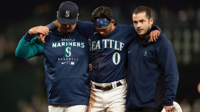 Seattle Mariners' Sam Haggerty, center, is helped off the field by training personnel manager Scott Servais, left, while stealing second base during the ninth inning of a baseball game against the Detroit Tigers, Monday, Oct. 3, 2022, in Seattle. The Tigers won 4-3. (Stephen Brashear/AP)