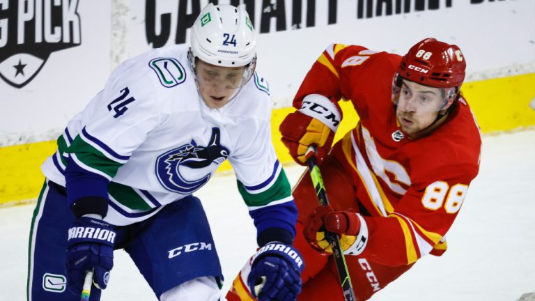 Vancouver Canucks defenceman Travis Dermott, left, gets past Calgary Flames left wing Andrew Mangiapane during first period NHL hockey action in Calgary, Saturday, April 23, 2022. (Jeff McIntosh/CP)