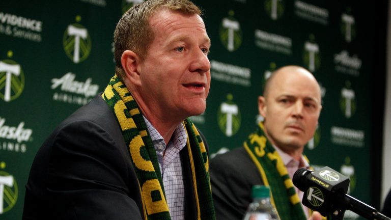 Portland Timbers team president and general manager Gavin Wilkinson, left, speaks as team owner Merritt Paulson, right, listens during an MLS soccer news conference on Jan. 8, 2018, in Portland, Ore. Wilkinson and Paulson have been removed from any decision-making roles with the Portland Thorn's National Women's Soccer League club until the findings are released from an ongoing investigation into numerous scandals around the league. (Sean Meagher/The Oregonian via AP)