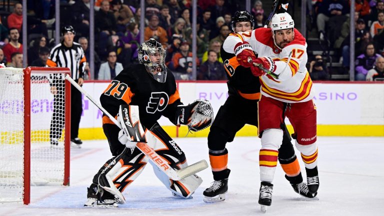 Philadelphia Flyers goaltender Carter Hart, left, looks for the puck past a screen from Travis Sanheim and Calgary Flames' Milan Lucic, right, during the first period of an NHL hockey game, Monday, Nov. 21, 2022, in Philadelphia. (Derik Hamilton/AP Photo)