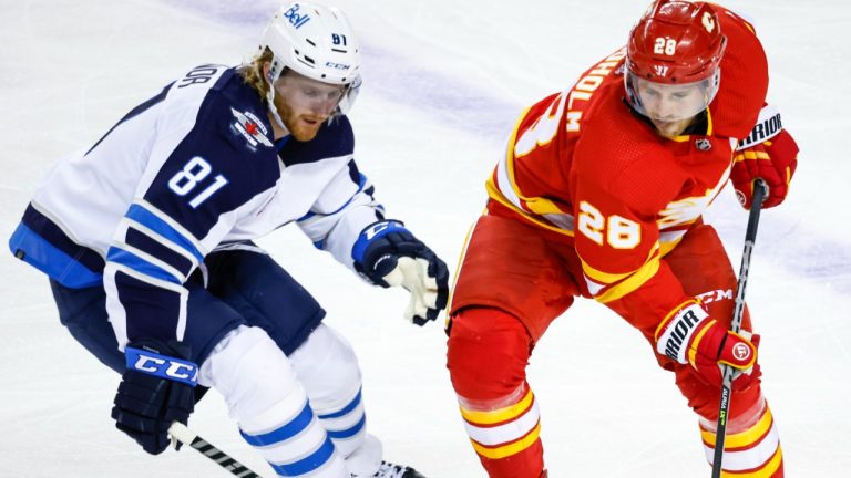 Winnipeg Jets forward Kyle Connor, left, and Calgary Flames forward Elias Lindholm battle for the puck during third period NHL pre-season hockey action in Calgary, Friday, Oct. 7, 2022. (Jeff McIntosh/CP)