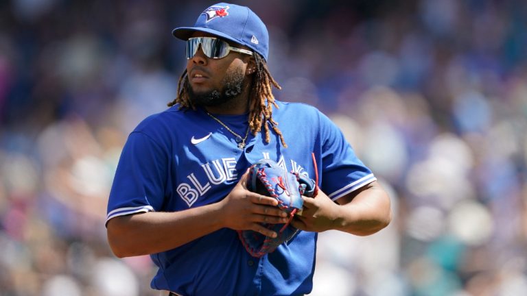 Toronto Blue Jays first baseman Vladimir Guerrero Jr. holds his glove after an apparent issue with its webbing as he walks to the dugout to get a new one after Seattle Mariners' Sam Haggerty (0) safely reached first during the fifth inning of a baseball game, Sunday, July 10, 2022, in Seattle. (Ted S. Warren/AP)