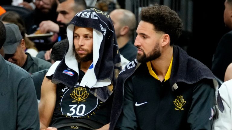 Golden State Warriors guard Stephen Curry, left, and guard Klay Thompson watch from the bench during the first half of an NBA basketball game against the Phoenix Suns, Wednesday, Nov. 16, 2022, in Phoenix. (AP Photo/Matt York)