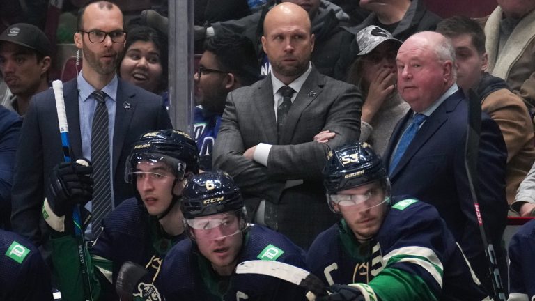 Vancouver Canucks head coach Bruce Boudreau, back right, stands on the bench with assistant coaches Jason King, back left, and Mike Yeo during the third period of an NHL hockey game against the St. Louis Blues in Vancouver, on Monday, December 19, 2022. (Darryl Dyck/CP)