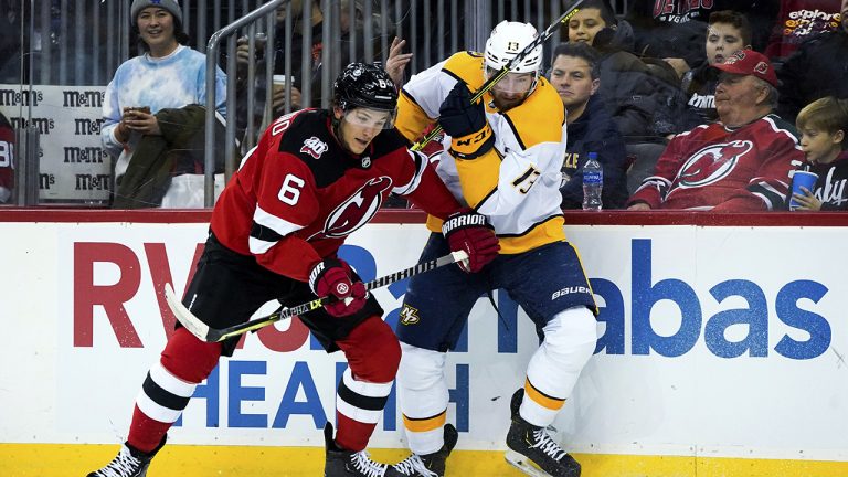 New Jersey Devils defenseman John Marino (6) pins Nashville Predators center Yakov Trenin (13) to the boards during the first period of an NHL hockey game Thursday, Dec. 1, 2022, in Newark, N.J. (Julia Nikhinson/AP)