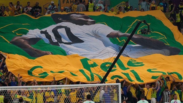 Soccer fans hold a giant Brazilian flag with picture of former Brazilian player Pele with message reads in English "Pele, Get well soon," during the World Cup group G soccer match between Cameroon and Brazil, at the Lusail Stadium. (Pavel Golovkin/AP)