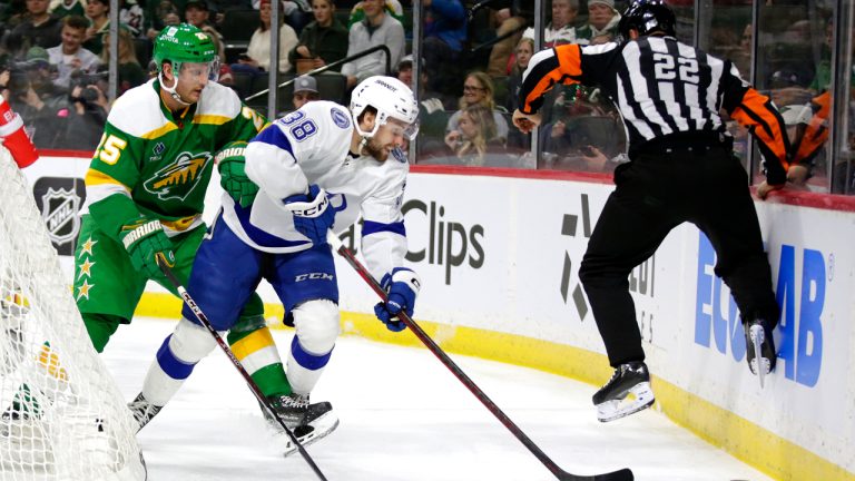 Tampa Bay Lightning left wing Brandon Hagel (38) and Minnesota Wild defenseman Jonas Brodin (25) go for the puck as official Ghislain Hebert (22) jumps out of the way of the puck the second period of an NHL hockey game Wednesday, Jan. 4, 2023, in St. Paul, Minn. (Andy Clayton-King/AP)