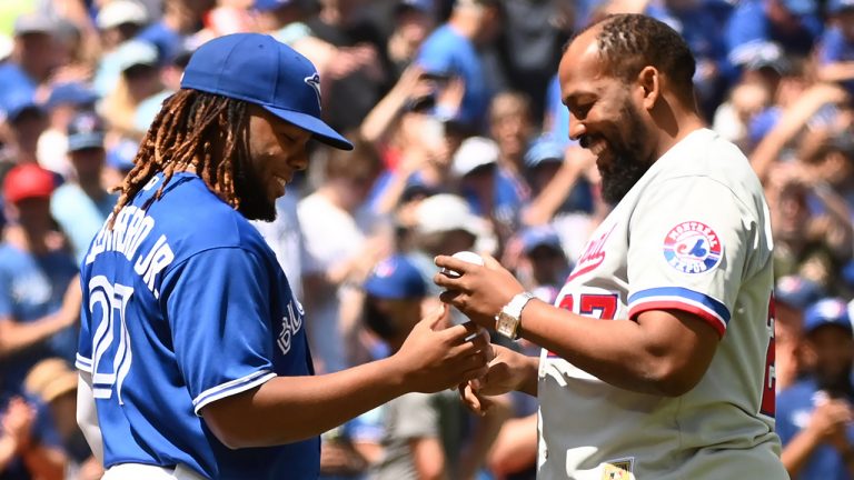 Vladimir Guerrero, right, signs a baseball with his son, Vladimir Guerrero Jr., after throwing out the ceremonial first pitch prior to American League baseball action between the Toronto Blue Jays and the Tampa Bay Rays in Toronto, Saturday, July 2, 2022. (Jon Blacker/CP)