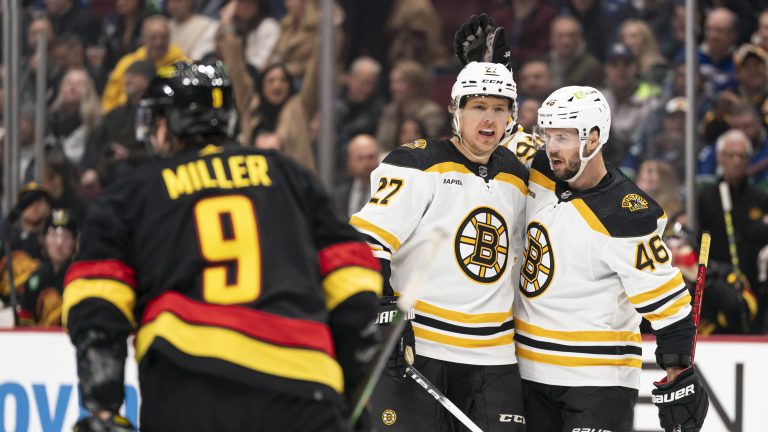 Boston Bruins' Hampus Lindholm (centre) is congratulated by teammate David Krejci (right) after scoring a goal as Vancouver Canucks' J.T. Miller sakes past during first period NHL hockey action in Vancouver, B.C., Saturday, February 25, 2023. (Rich Lam/CP)