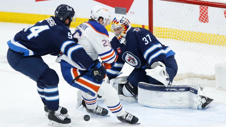 Winnipeg Jets goaltender Connor Hellebuyck (37) pokes the puck away from Edmonton Oilers' Mattias Janmark (26) as Dylan Samberg (54) defends during first period NHL action in Winnipeg, Saturday, March 4, 2023. (John Woods/CP)