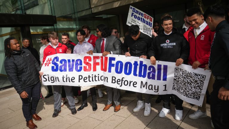 Simon Fraser University football team players hold a banner after attending a hearing at B.C. Supreme Court, in Vancouver, on Monday, May 1, 2023. The lawyer representing players and alumni of Simon Fraser University's football team asked a judge to grant an injunction that would require the university to attempt to bring back the axed program. (Darryl Dyck/CP)