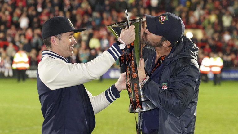 Wrexham co-owners Rob McElhenney, left, and Ryan Reynolds celebrate with the trophy after their team clinched promotion following the National League soccer match between Wrexham and Boreham Wood at The Racecourse Ground, in Wrexham. (Martin Rickett/AP)