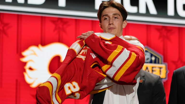 Samuel Honzek puts on a Calgary Flames jersey after being picked by the team during the first round of the NHL hockey draft Wednesday, June 28, 2023, in Nashville, Tenn. (AP)