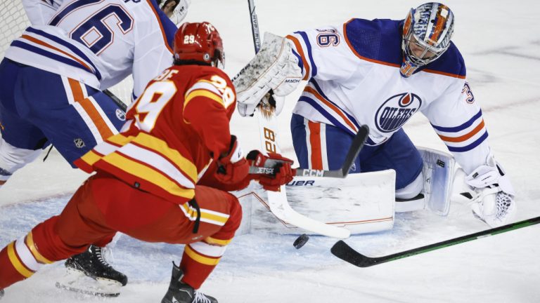 Edmonton Oilers goalie Jack Campbell, right, swats the puck away from Calgary Flames forward Dillon Dube during first period NHL preseason hockey action in Calgary, Alta., Friday, Sept. 29, 2023. (Jeff McIntosh/CP)