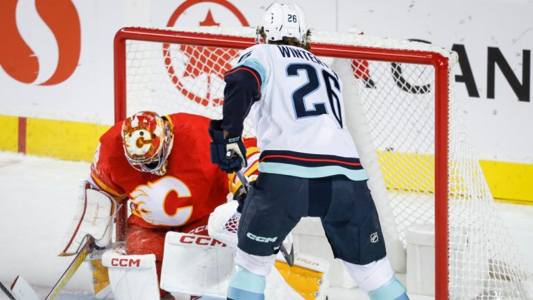 Seattle Kraken forward Ryan Winterton, right, looks on as Calgary Flames goalie Dustin Wolf covers the puck during first period NHL preseason hockey action in Calgary, Monday, Sept. 25, 2023. (Jeff McIntosh/CP)