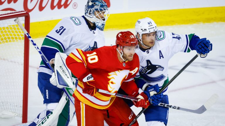 Vancouver Canucks' Noah Juulsen, right, checks Calgary Flames forward Jonathan Huberdeau, centre, as Canucks goalie Artors Silovs looks on during first period NHL preseason hockey action in Calgary, Sunday, Sept. 24, 2023. (Jeff McIntosh/CP)