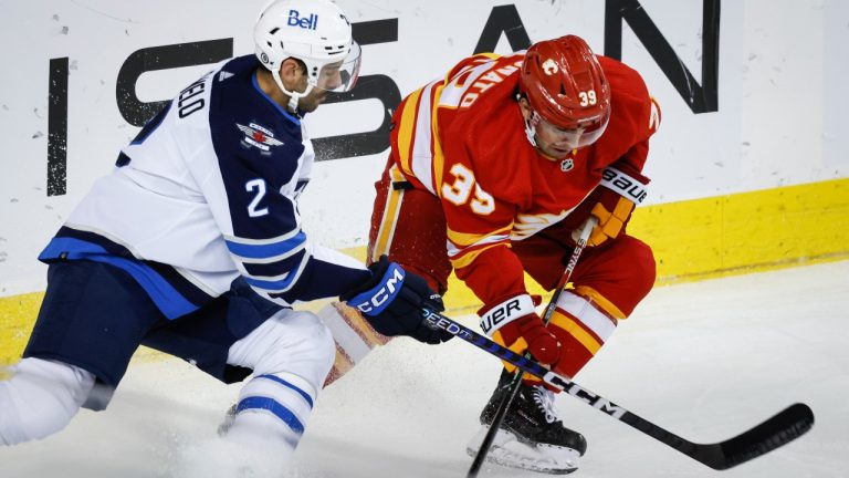 Winnipeg Jets defenceman Dylan DeMelo, left, swats the puck away from Calgary Flames forward Matthew Coronato during first period NHL preseason hockey action in Calgary, Alta., Monday, Oct. 2, 2023. (Jeff McIntosh/THE CANADIAN PRESS)