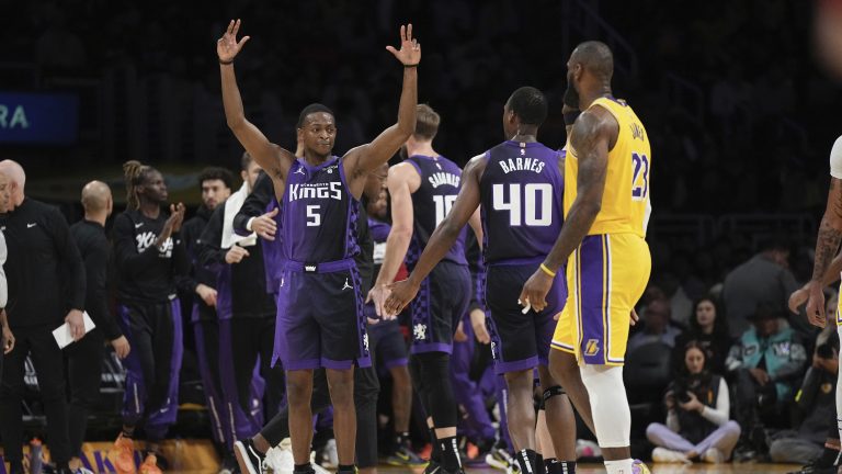 Sacramento Kings guard De'Aaron Fox, left, celebrates with forward Harrison Barnes, center, as Los Angeles Lakers forward LeBron James looks on after a timeout was called during the first half of an NBA basketball game Wednesday, Nov. 15, 2023, in Los Angeles. (Mark J. Terrill/AP)